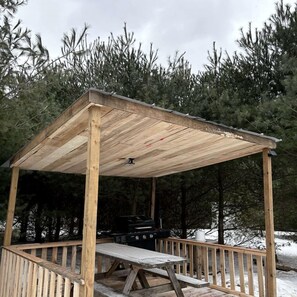 Un kiosque en bois avec un banc et un espace barbecue.