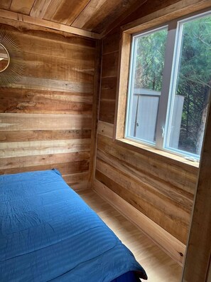 Une pièce de cabane en bois comprenant un lit, une fenêtre et une décoration murale en forme de soleil rayonnant.