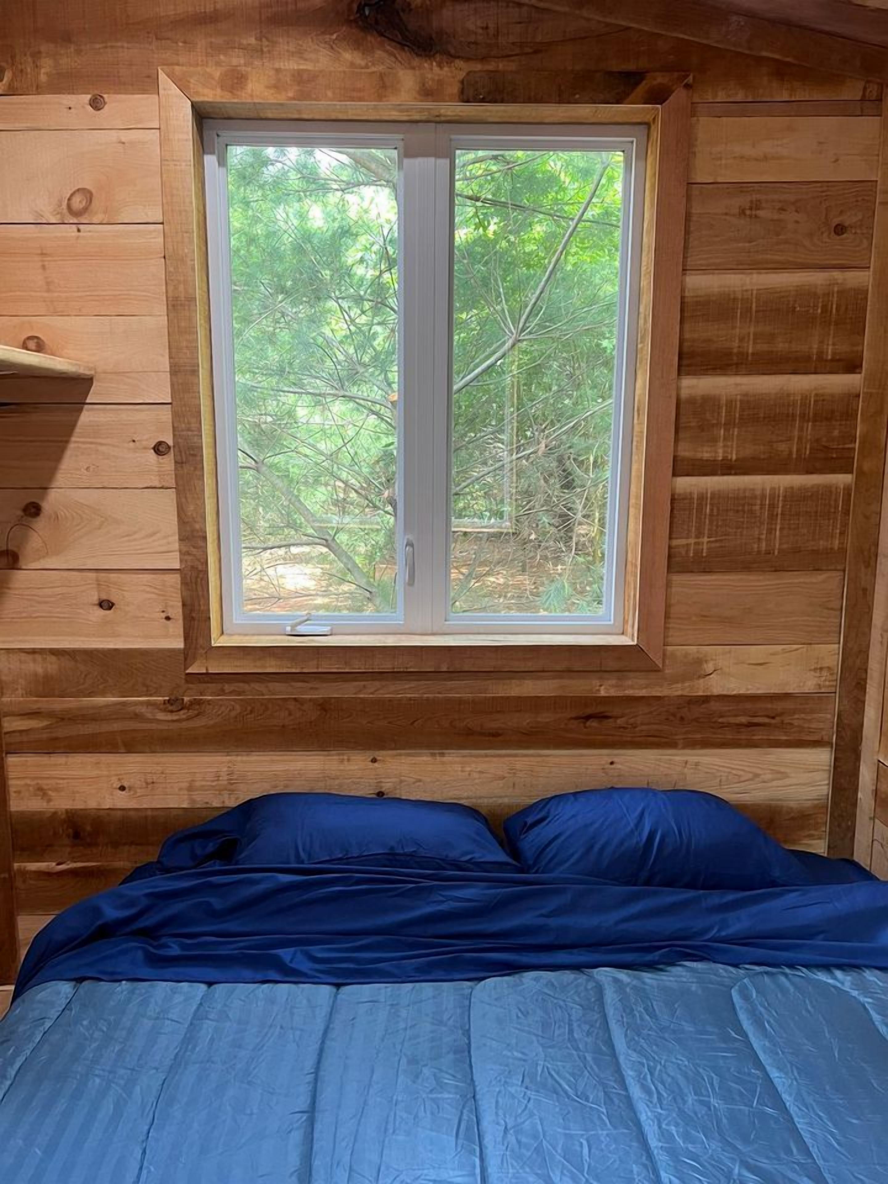 A wooden cabin room with a bed, a window, and a shelf.