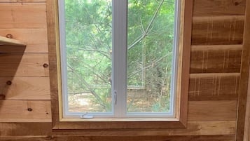 A wooden cabin room with a bed, a window, and a shelf.