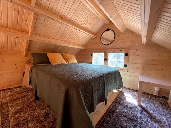 A cozy wooden room with a bed, a small table, and a window.