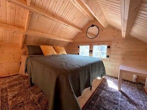 Ein gemütliches Zimmer aus Holz mit einem Bett, einem kleinen Tisch und einem Fenster.