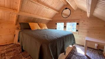 Ein gemütliches Zimmer aus Holz mit einem Bett, einem kleinen Tisch und einem Fenster.