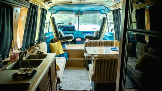 Un intérieur de camping-car compact comprenant un coin cuisine, un espace salon et une vue par les fenêtres.