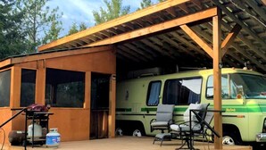 Un espace extérieur abrité comprenant un fourgon vert, un barbecue et un coin salon.