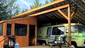 Un espace extérieur abrité comprenant un fourgon vert, un barbecue et un coin salon.