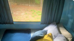A bed with a blue mattress, a pillow, and a yellow pillow. - Vintage Airtstream with Large Roofed Deck, BBQ, Fire Pit and Forest Views in Ontario (Blackstock)