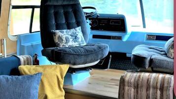 Interior acogedor de una caravana, con un sofá azul, una mesa de comedor con platos y una taza, y una butaca negra con capitonado.