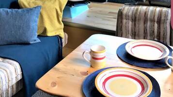 A cozy RV interior with a blue couch, a dining table with plates and a mug, and a black tufted chair.