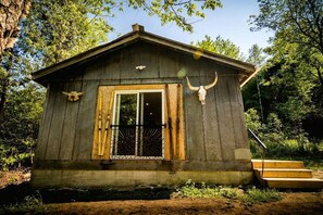 Une cabane rustique avec une façade en bois, une porte d’entrée, un petit porche et un escalier menant à l’entrée.