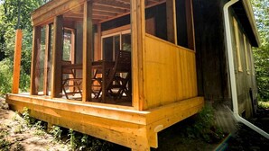 Une cabane en bois dotée d’un porche couvert, d’un coin repas avec des chaises et d’un petit abri attenant.