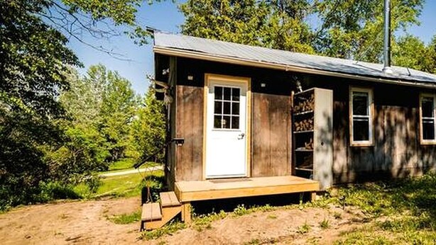 Una pequeña cabaña de madera con puerta principal, ventanas y un porche.