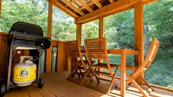 A wooden deck with a grill and propane tank, two wooden chairs, and a table.