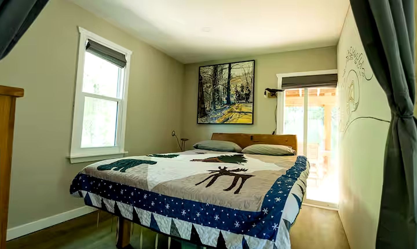 Un dormitorio con cama, un cuadro, una ventana y cortina.