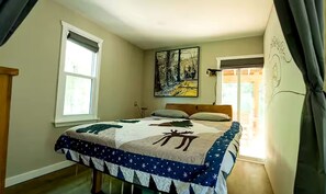 A bedroom with a bed, a painting, a window, and a curtain.