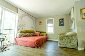 Une chambre à coucher avec un lit, une chaise, une fenêtre et des œuvres d’art accrochées aux murs.