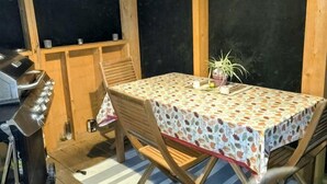 Un patio al aire libre con una mesa cubierta con un mantel estampado, sillas de madera, una parrilla y una planta en maceta.