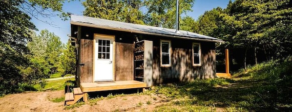 Une petite cabane en bois avec une porte d’entrée, des fenêtres et une véranda.
