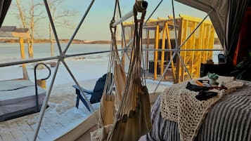 Ein Zelttraum mit Blick auf einen zugefrorenen See, eine Hängematte, ein Bett mit Strickdecke und eine Holzterrasse im Freien.
