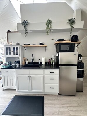 A compact kitchen with white cabinets, a black countertop, a stainless steel refrigerator, and a microwave.