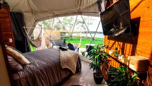 Un hébergement sous tente comprenant un lit, un hamac, une télévision et une vue sur l’extérieur.