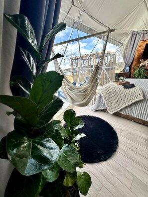 A tent with a hammock, a large plant, a round rug, and a bed with a knitted blanket.
