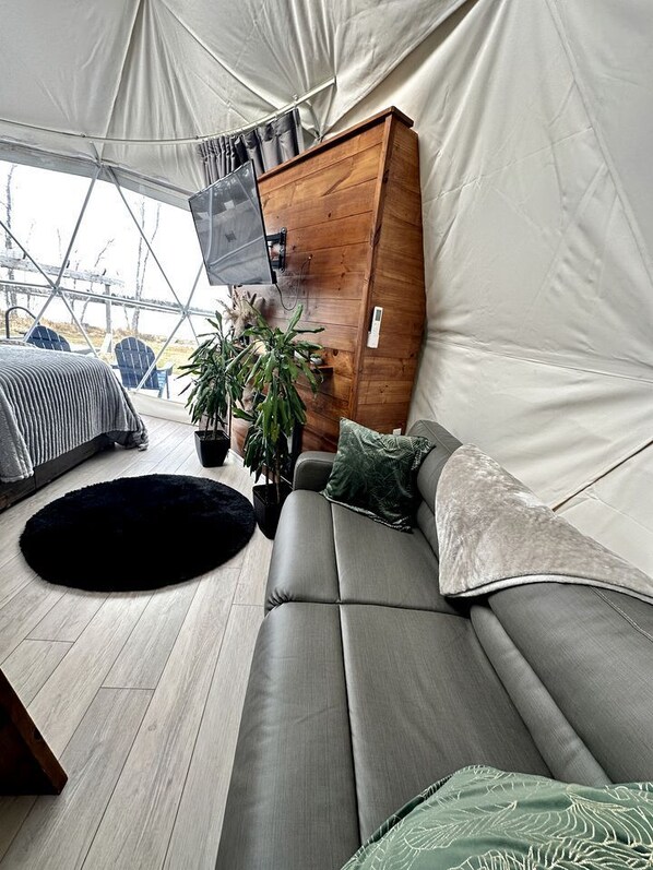 A tented living area with a sofa, a black rug, a wooden cabinet, and a potted plant.