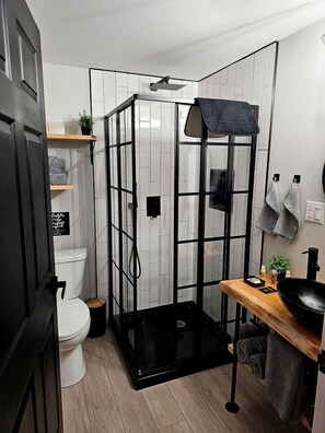 A compact bathroom with a shower enclosure, toilet, and a sink area with towels and toiletries.