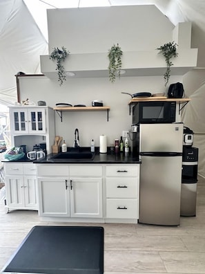 A compact kitchen with white cabinets, a black countertop, a stainless steel refrigerator, and a microwave.