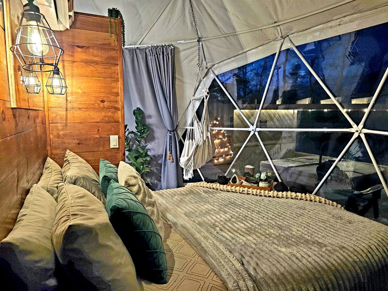Une pièce aménagée comme une tente, avec un lit, des oreillers, un luminaire suspendu et une vue par la fenêtre.