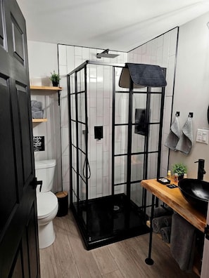 Baño compacto con cabina de ducha, inodoro y zona de lavabo con toallas y artículos de aseo.