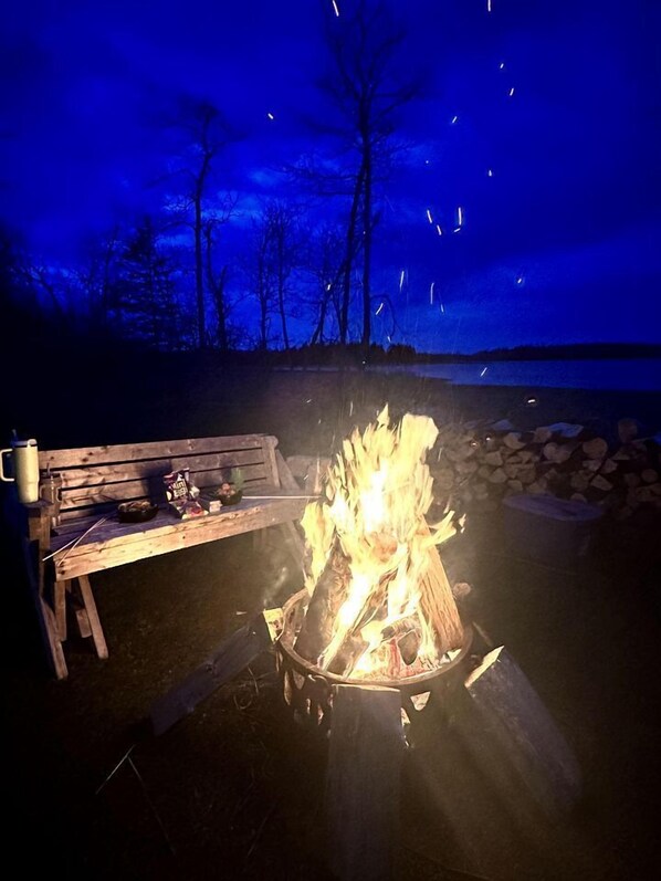 A campfire with a bench and a table with snacks, set against a night sky.