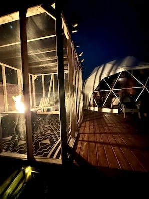 A covered outdoor area with a wooden deck and a glass enclosure with a fire.
