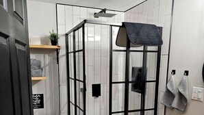 A compact bathroom with a shower enclosure, toilet, and a sink area with towels and toiletries. - Cozy Dome Rental in Canada, for Romantic Weekends in Nature in Nova Scotia (Antigonish)