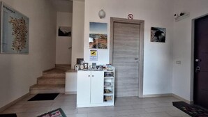 Un couloir avec un escalier, une armoire blanche contenant divers objets et une porte sur laquelle est apposé un panneau «interdiction de fumer».