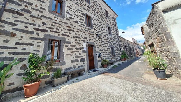 Un bâtiment en pierre, de style architectural traditionnel, avec une rue étroite et des plantes en pot le long du trottoir.