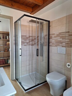 Ein modernes Badezimmer mit Duschkabine aus Glas, einer weißen Toilette und einem Holzregal mit Büchern.