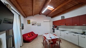 Une cuisine compacte avec des meubles rouges, une table à manger avec des chaises, un canapé rouge et un téléphone sur le côté gauche.