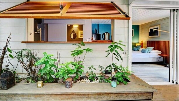 Een modern interieur met een houten lambrisering, diverse potplanten en een blik op een slaapkamer met een bed en een televisie.