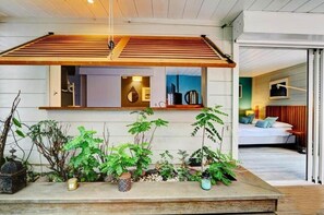 Ein modernes Interieur mit einer Holz-Schubladen-Decke, verschiedenen topfgepflanzten Pflanzen und einem Blick in einen Schlafbereich mit Bett und Fernseher.
