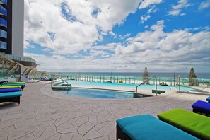 Ein Poolbereich auf dem Dach mit Blick auf den Ozean, Liegestühle und eine moderne Gebäudeanlage.