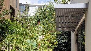 A narrow outdoor corridor with dense foliage on one side and a building entrance on the other. - MAMAD - Chic and Comfort stay on Iconic (Tel Aviv)