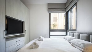 A modern hotel room with a large bed, a flat-screen TV, and a window with a view of the outside. - MAMAD - Chic and Comfort stay on Iconic (Tel Aviv)