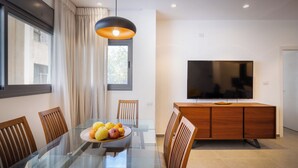 A modern dining area with a glass table, wooden chairs, and a fruit bowl. - MAMAD - Chic and Comfort stay on Iconic (Tel Aviv)
