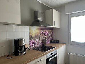 A modern kitchen with a built-in stove, a coffee maker, and a window with blinds. - Apartment Flieder, 95 sqm with Balcony (Herscheid)