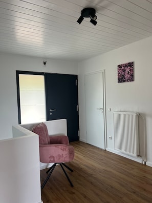 Een kamer met een houten vloer, een witte radiator, een deur en een raam met zonwering.