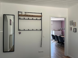 Een kamer met een spiegel, een wandplank met haken, en een deur naar een andere kamer.