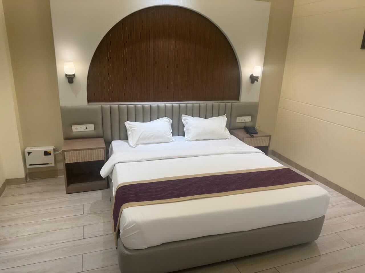 A hotel room with a large bed, a headboard, bedside tables, and a wall-mounted light fixture.