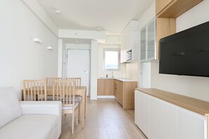 Un espace de vie compact comprenant un coin cuisine, un coin repas et un téléviseur fixé au mur.