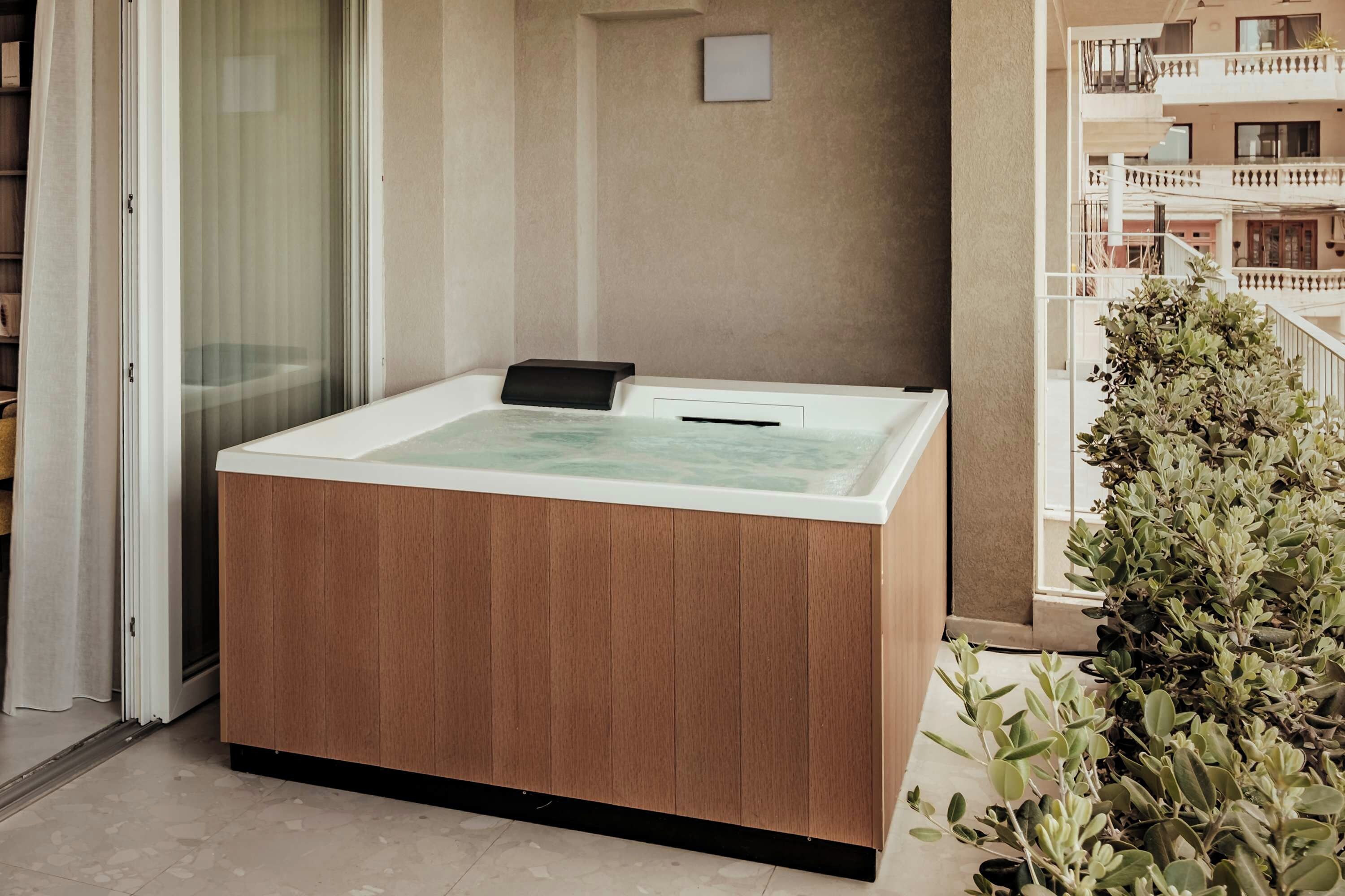Un espace spa comprenant une baignoire en bois, une porte en verre et un balcon agrémenté de plantes.